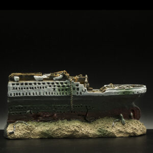 Damaged model cruise ship resting on a rocky base, with broken decks and a dark hull.