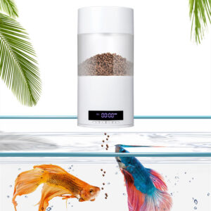 Automatic fish feeder dispensing pellets into a home aquarium, with orange and blue fish swimming below and palm fronds in the background.