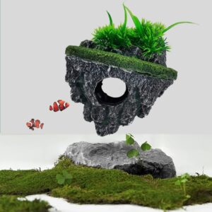 Decorative aquarium ornament: a dark hollow rock with a circular hole, moss and green plants on top, with two clownfish nearby; mossy rocks below.