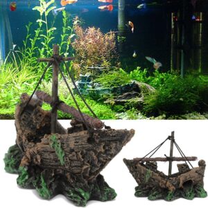 Decorative aquarium shipwreck ornament: brown, weathered sailing ship perched on green rocky base with ropes and masts in front of live plants and fish tank backdrop.